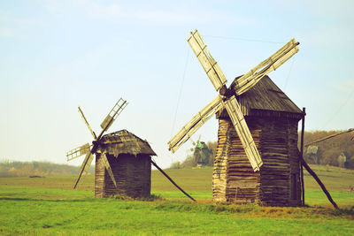 Two old wooden windmills with a broken roof on a green field