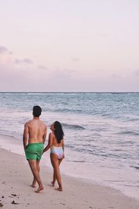 Man and woman walking on shore against sea at beach