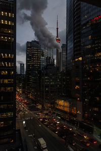 Cars on street by illuminated city against sky