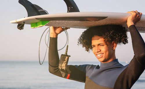 Young latino surfers carrying surfboard on head with sea in background. a cheerful young afro. 