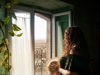 Side view of woman looking through window at home