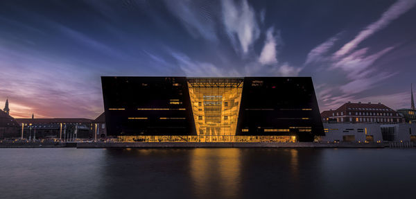 Illuminated buildings by river against sky at night