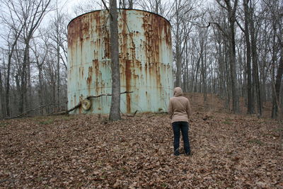 Rear view of woman standing against rusty water tank on field in forest