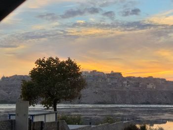 Scenic view of river by buildings against sky during sunset