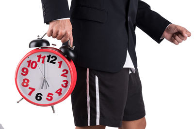 Midsection of businessman holding alarm clock against white background