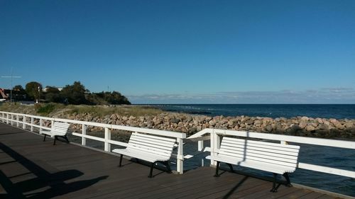 Deck chairs on beach against clear blue sky