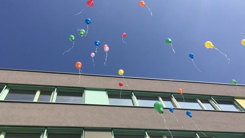 Low angle view of balloons against building against blue sky