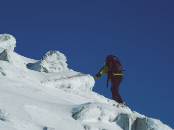 Man skiing on snowcapped mountain against clear blue sky