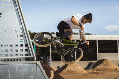 Young man jumping with bicycle at bike park on sunny day