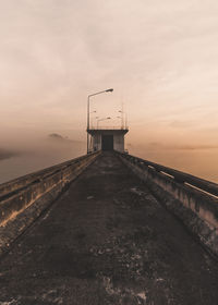 Diminishing perspective of footbridge over sea against sky during sunset