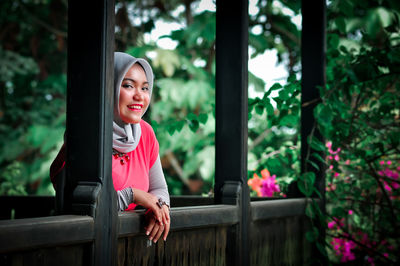 Portrait of smiling young woman standing by railing