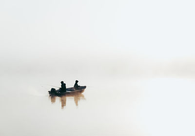 Man and child fishing in a boat in very heavy fog on a lake.