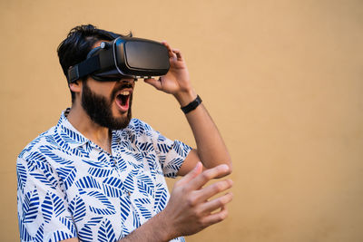 Young man using virtual reality simulator while standing by wall outdoors