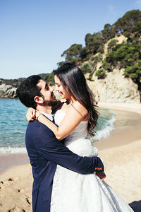 Happy newlywed couple romancing at beach against clear sky