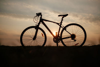 Silhouette bicycle on field against sky during sunset