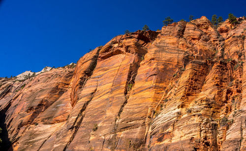 Low angle view of rocky mountains against clear blue sky