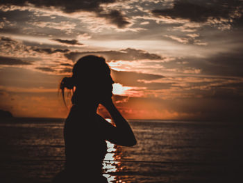 Silhouette woman standing by sea against sky during sunset