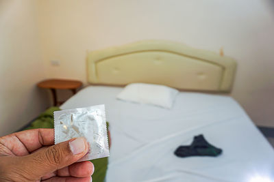 Cropped hand holding condom packet in bedroom