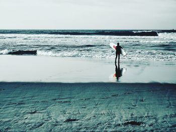 Rear view of man standing at beach against sky