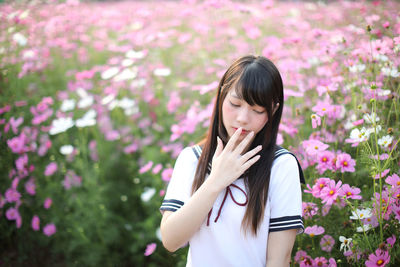 Beautiful young woman standing by pink flowering plants