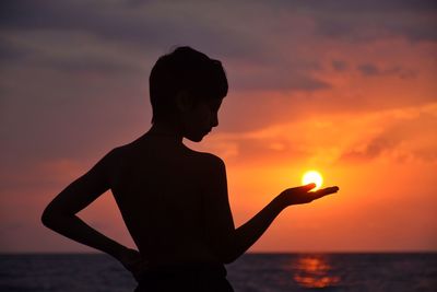Silhouette boy standing against sea during sunset