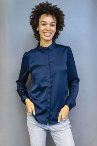 Smiling businesswoman with hands in pockets standing against blue background