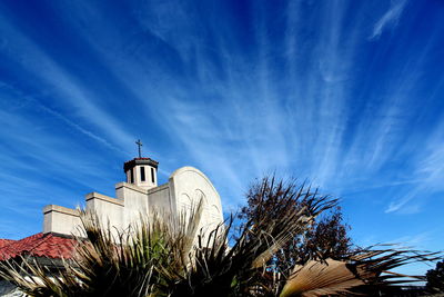 Church steeple, with light rays behind and palm fronds in foreground.