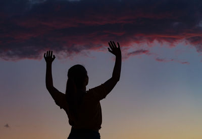 Silhouette woman with arms raised against sky during sunset