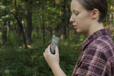 Side view of woman holding burning sage against trees at forest