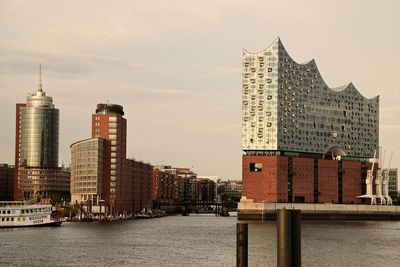 View of buildings by river against sky in city