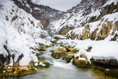 Scenic view of stream amidst snowcapped mountains during winter