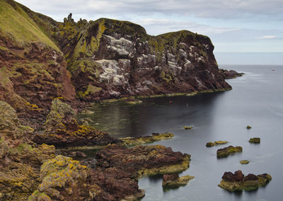 Scenic view of rocks by sea against sky