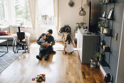 High angle view of father holding autistic son while sitting by daughter on floor at home