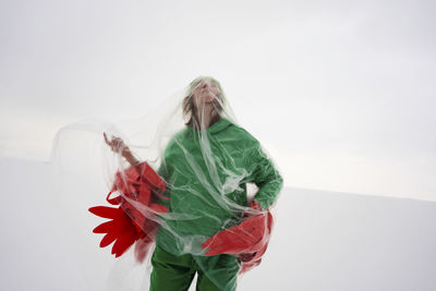 Suffocated woman wearing bird costume wrapped in plastic against sky