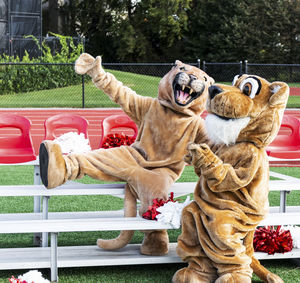 Male and female cougar mascots fool around for the camera while sitting on small portable bleachers