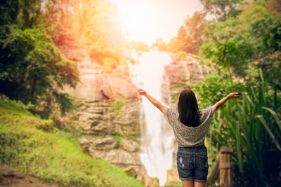 Rear view of woman with arms outstretched standing against plants