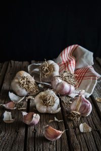 Close-up of pink garlic bulbs and cloves on rustic wooden table with black background