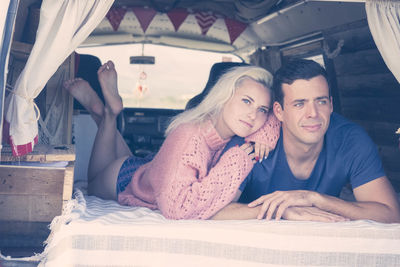 Thoughtful couple looking away while lying on bed in motor home