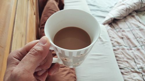 Cropped hand holding coffee cup in bedroom at home