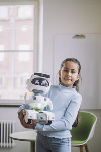 Portrait of girl carrying social robot standing in innovation lab