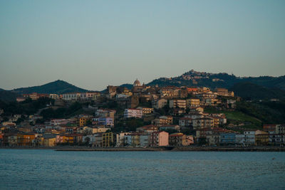 Houses on mountain by sea against clear sky during sunset