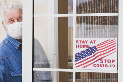 Portrait of senior man wearing mask standing at house entrance