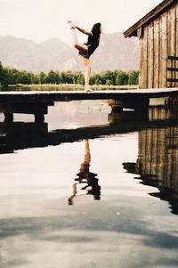 Full length of woman practicing yoga over lake against mountain