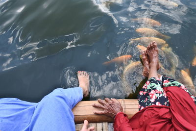 Low section of women sitting on pier over lake