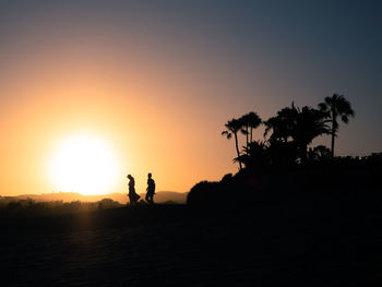 Silhouette people by palm trees against sky during sunset