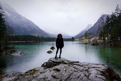 Man standing on rock by lake against sky