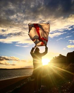 Silhouette woman standing with english flag at beach against sky during sunset