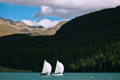 Sailboat sailing on lake by mountains against sky