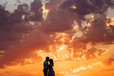 Silhouette couple photographing against sky during sunset