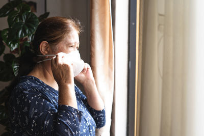 Woman wearing mask looking through window at home